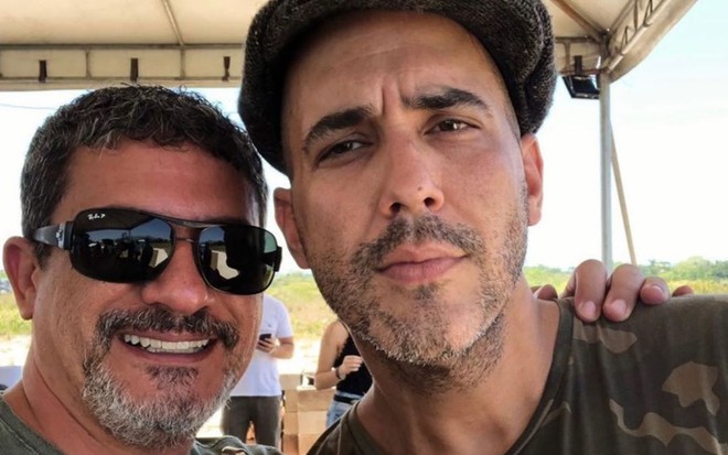 Tom Veiga de óculos escuros e André Marques de luva laranja, lado a lado, posando para foto