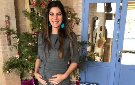 Andréia Sadi em foto sorridente mostrando a barriga de grávida