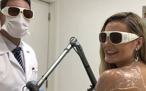 Andressa Urach de óculos de proteção sentada em frente ao médico que realizava a remoção das tatuagens