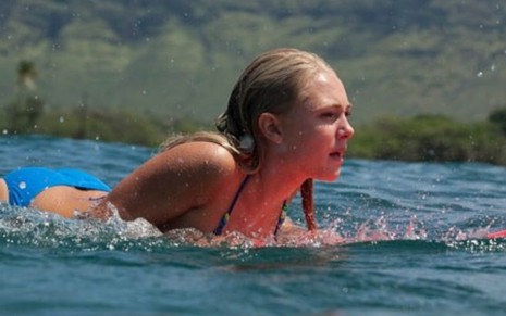 No mar, a atriz AnnaSophia Robb surfa deitada na prancha em cena como Bethany no filme Coragem de Viver (2011)