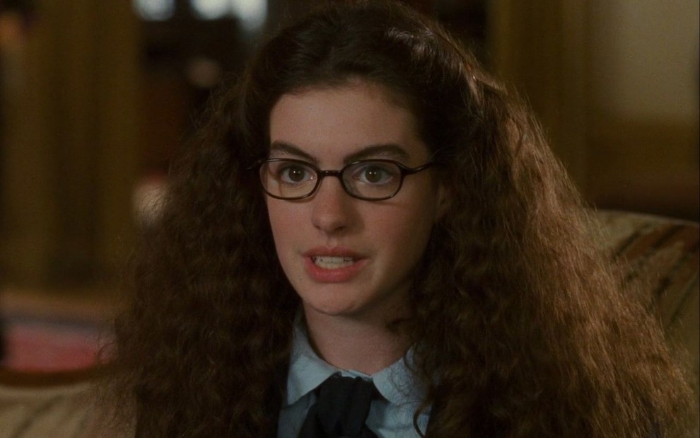 Anne Hathaway usa óculos e está com os cabelos crespos em cena como Mia de O Diário da Princesa (2002)