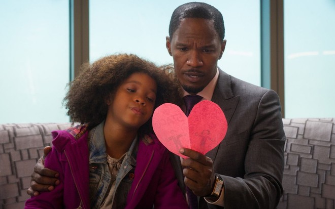 Quvenzhané Wallis encosta a cabeça no ombro de Jamie Foxx, que segura um coração de papel na mão em cena de Annie (2014)