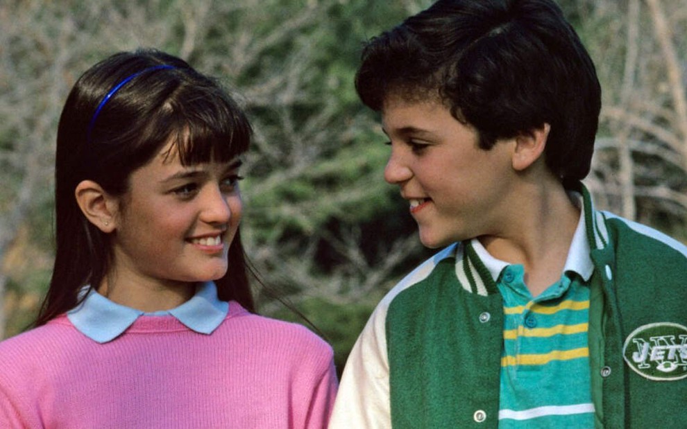 De blusa rosa, Danica McKellar sorri para Fred Savage, com um casaco esportivo, enquanto andam de mãos dadas em Anos Incríveis