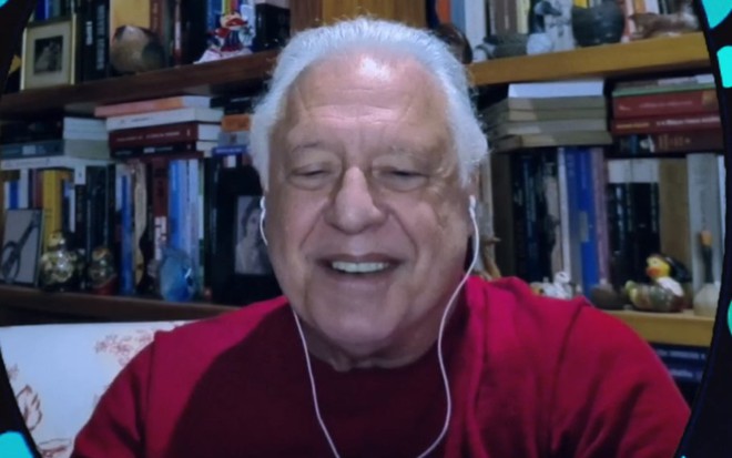 Antonio Fagundes com uma camiseta vermelha em um cenário com livros ao fundo