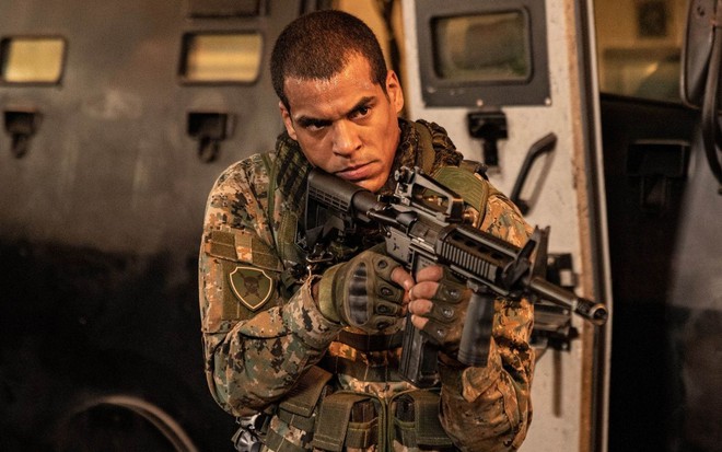 Vestido com uniforme do Exército, Marcello Melo Jr. segura uma arma em cena da série Arcanjo Renegado