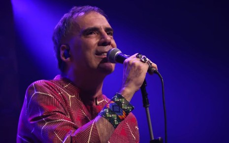 Arnaldo Antunes de roupa colorida segurando microfone durante show