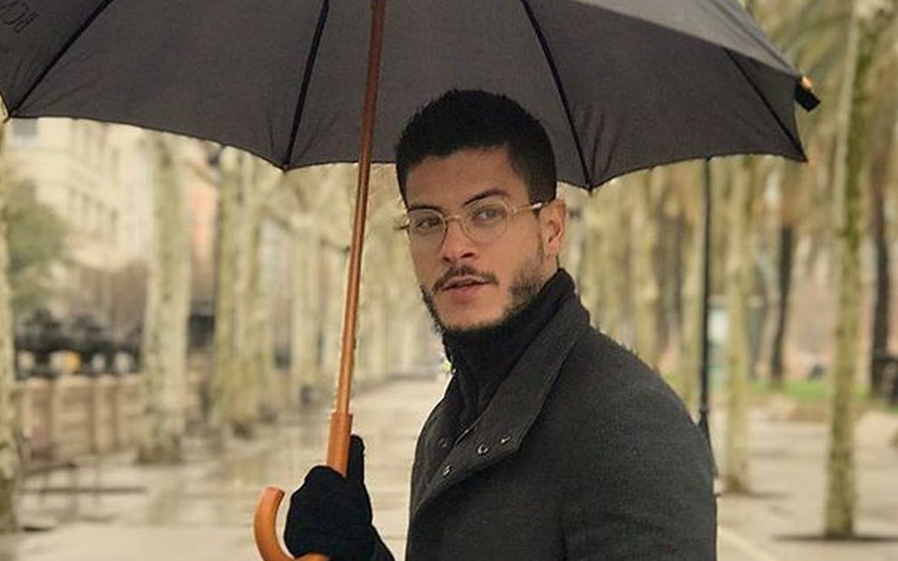 Arthur Aguiar sério com um guarda-chuva na mão