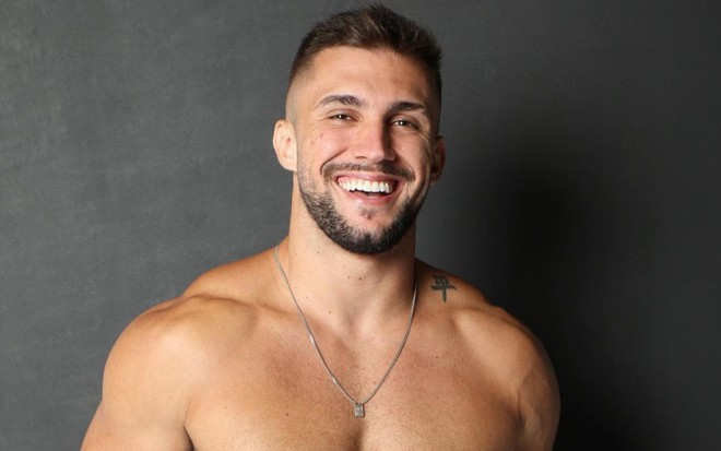 Arthur Picoli sorrindo, sem camisa, e com uma corrente no pescoço
