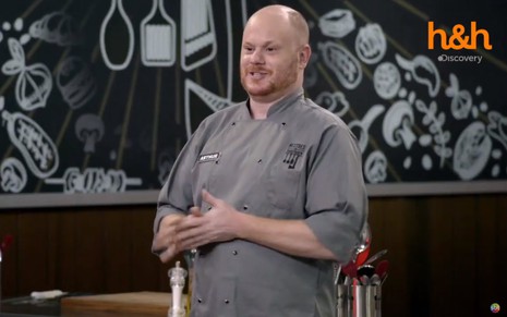 Arthur Sauer no cenário do Mestres da Sabotagem, programa de culinária do SBT; ele usa uniforme de cozinheiro cinza