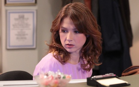 Erin Hannon (Ellie Kemper) em cena de The Office de blusa rosa atrás de uma mesa de escritório
