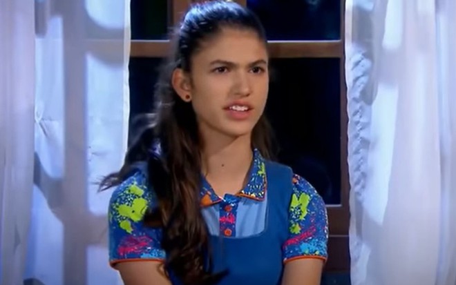Mili (Giovanna Grigio) em cena de Chiquititas, com vestido azul estampado e cabelo preso para trás