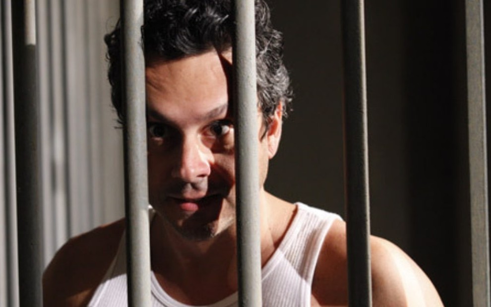 O ator Alexandre Nero com expressão de raiva atrás das grades da cadeia