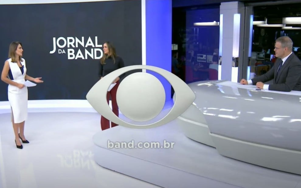 Encerramento do Jornal da Band, com o logo da emissora em destaque; Lana Canepa, Paloma Tocci e Eduardo Oinegue estão ao fundo