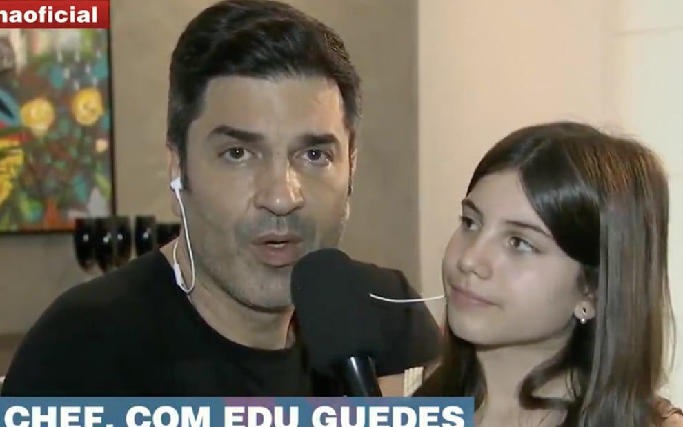 Com fones de ouvido, Edu Guedes segura um microfone com a filha Maria Eduarda Guedes ao lado