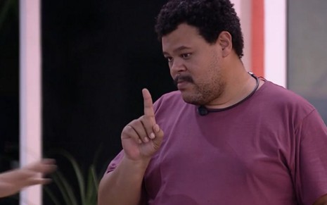 Imagem de Babu Santana de camiseta roxa e com o dedo indicador apontando para cima