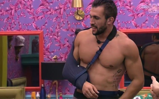 Imagem de Arthur Picoli sem camisa e de tipoia no quarto colorido do BBB21