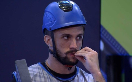 Arthur olha para o lado, está com capacete azul e uma mão na boca