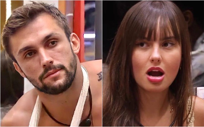 Arthur está sem camiseta, está com o braço imobilizado com a tipoia branca; Thaís está com o cabelo, olha para o lado e está de boca aberta