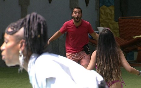 Gilberto Nogueira (ao fundo da imagem) grita no jardim do BBB21; Karol Conká, em primeiro plano, conversa