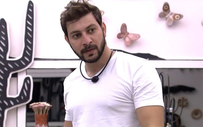 Imagem de Caio Afiune no quarto cordel do BBB21; rapaz usa camiseta branca apertada