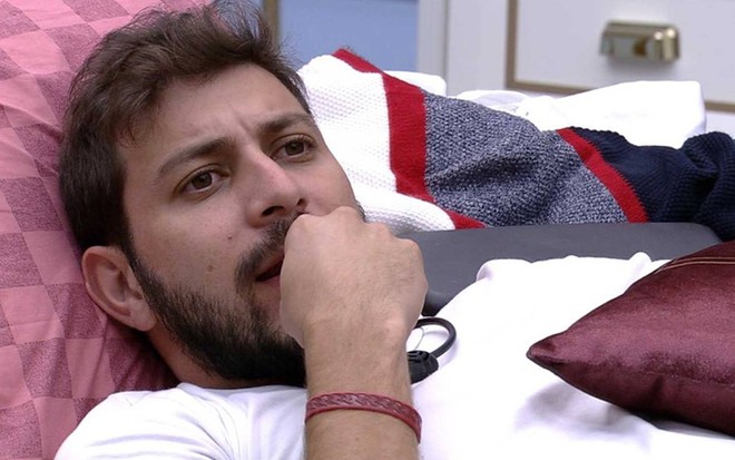 Caio está deitado, olha para cima e usa camiseta branca