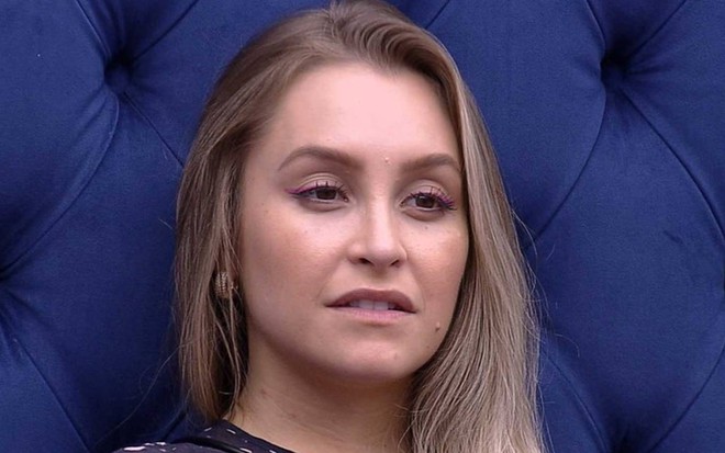 Carla Diaz está encostada na cama azul, olha para frente e está com o cabelo solto