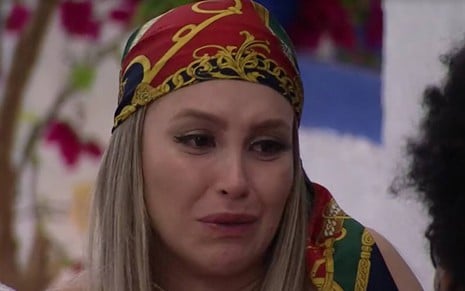Carla chora, usa lenço vermelho e verde na cabeça e está com o cabelo solto