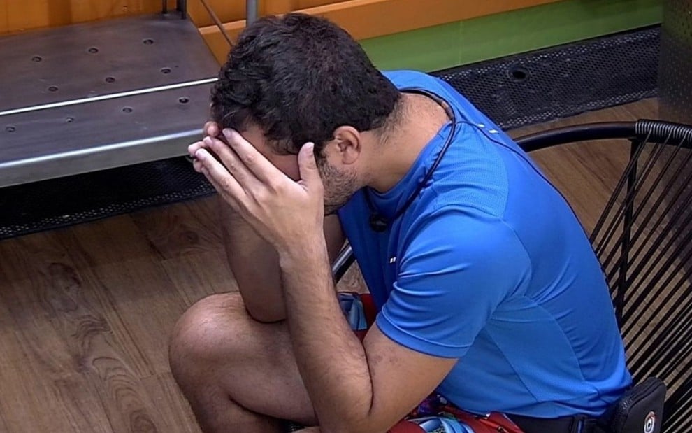 Sentado, Gilberto Nogueira cobre o rosto com as mãos enquanto chora no BBB21