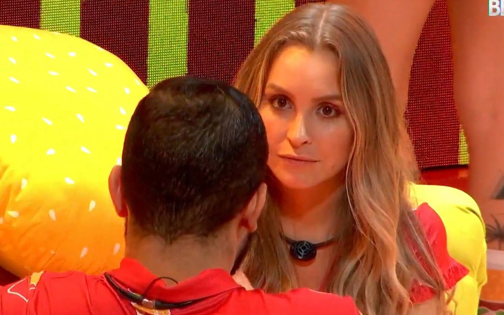 Gilberto está de costas, usa camiseta vermelha; Carla olha para o brother, está com o cabelo solto e usa camiseta vermelha