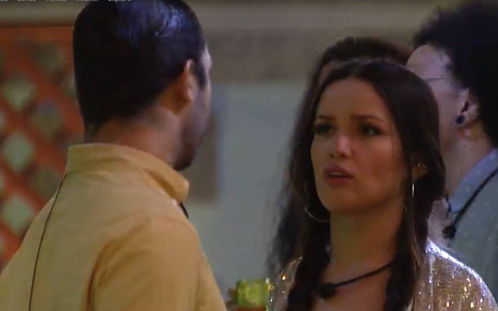 Gilberto olha para Juliette; ele usa camiseta amarela; a sister olha para o brother; ela está com o cabelo trançado e usa casaco branco brilhante