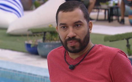 Gilberto Nogueira no BBB21 com camisa vermelha sentado na área externa