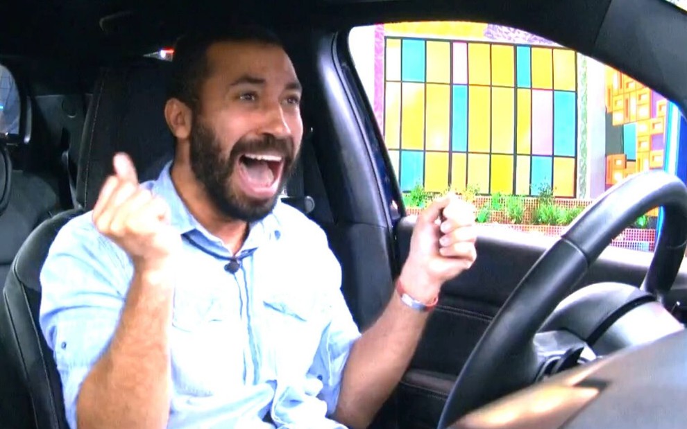Dentro de um carro no BBB21, Gilberto Nogueira está com a boca aberta gritando de alegria