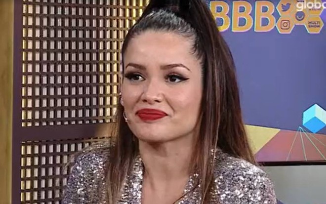 Juliette olha para o lado, está com o cabelo preso, usa macacão prata e batom vermelho