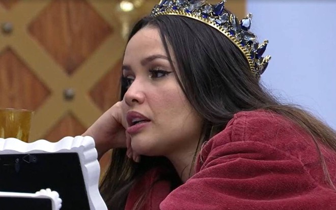 Juliette está deitada, usa roupão vermelho e coroa na cabeça