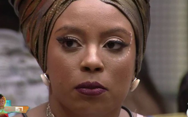 Lumena olha para o lado, usa batom roxo e está com lenço dourado no cabelo