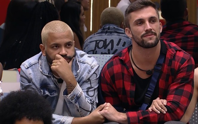 Imagem de Projota (à esq.) e Arthur Picoli de mãos dadas na sala do BBB21