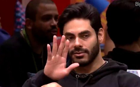 Rodolffo levanta a mão em sinal de desculpa para as câmeras no BBB21, da Globo