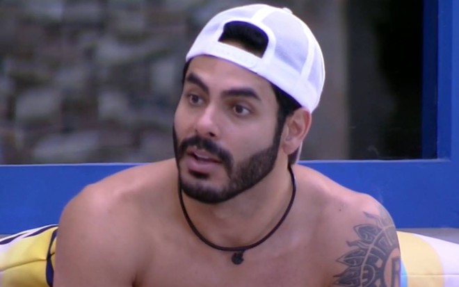 Rodolffo está sentado, sem camiseta e usa boné branco