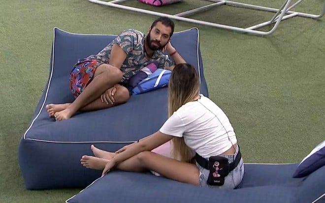 Imagem de Gilberto Nogueira e Sarah Andrade, de costas, conversando na área externa do BBB21