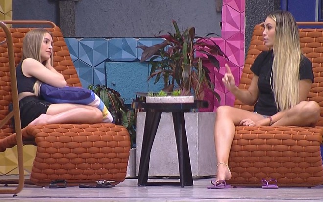Imagem de Carla Diaz e Sarah Andrade sentadas em cadeiras localizadas na área externa do BBB21