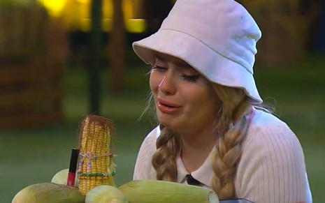 Viih Tube olha para um milho, ela chora e usa boné branco e camiseta branca