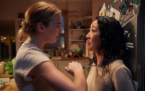 Jodie Comer e Sandra Oh caracterizadas como Vilannelle e Eve em cena de Killing Eve: Jodie aponta uma faca em direção ao peitoral de Sandra Oh e a encurrala na porta de uma geladeira