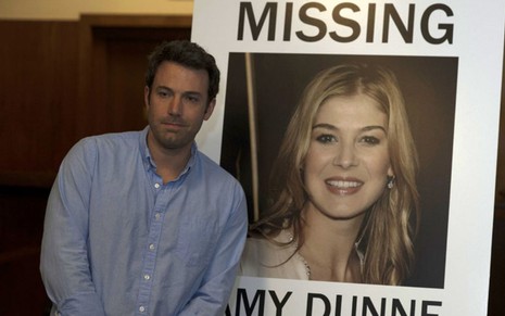 Nick (Ben Affleck) parece desconfortável em frente ao cartaz de desaparecida de Amy (Rosamund Pike) em Garota Exemplar