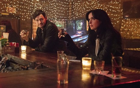 Benjamin Walker e Krysten Ritter bebem em um bar em cena da série Jessica Jones