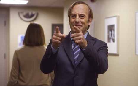 Com um sorriso maroto no rosto, Bob Odenkirk aponta os dedos em gesto descontraído na quinta temporada de Better Call Saul