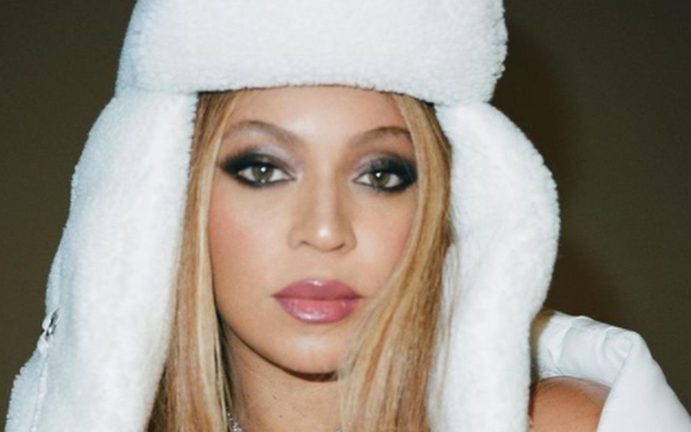 Beyoncé de chapéu branco e felpudo, colar prata e batom de cor neutra