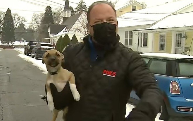 Bob Barnard, repórter da FOX 5 DC, de casaco preto e máscara da mesma cor, com o cachorrinho marrom no colo
