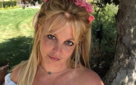 Britney Spears, loira, de franja, coroa de flores rosas na cabeça e blusa xadrez