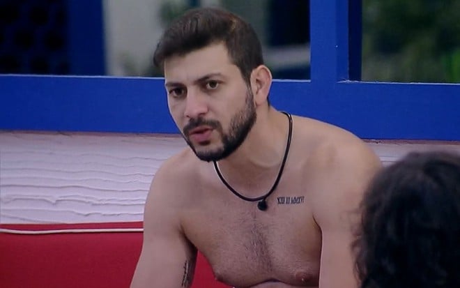 Caio Afiune pensativo durante conversa com Fiuk, que não aparece na imagem, na área externa do BBB21