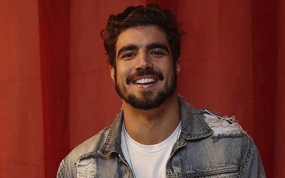 Caio Castro sorrindo, usando jaqueta jeans